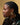 A woman with braided hair wearing the gold tone hoop earrings, set against a yellow background.