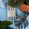 Recycled cotton paper decoration with striped pattern on a blue surface, surrounded by green leaves.