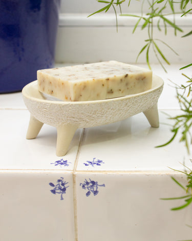 Bar of soap on an AARVEN handmade white soapstone soap dish on a tiled surface.