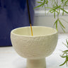 Handmade white soapstone incense holder with an AARVEN incense stick on a tiled surface, with a plant in the background.