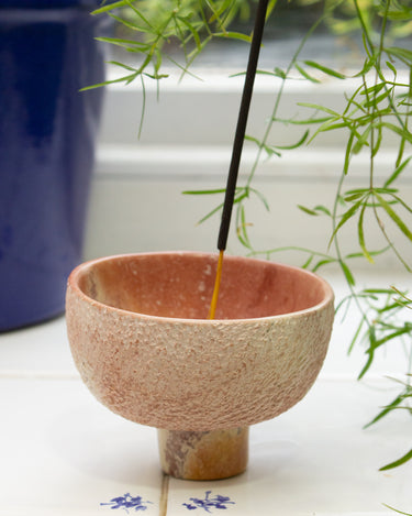 Handmade ceramic incense burner with a lit AARVEN incense stick on a tiled surface, with a plant in the background.
