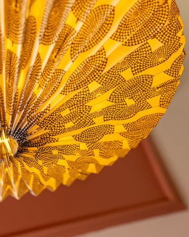 A close-up of AARVEN Black Sun Mask paper light shade with intricate black geometric patterns, shown against a warm teracotta background.