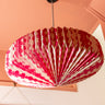 AARVEN paper pendant light with a pink pattern of dots, hanging from a black ceiling canopy in a peach-colored room.