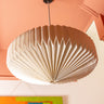 AARVEN large, pleated paper pendant light shade in a warm off-white color, suspended from a black ceiling mount against a peach-coloured ceiling.