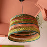 Colorful woven lampshade hanging against a pink wall.