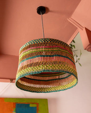 Colorful woven lampshade hanging against a pink wall.