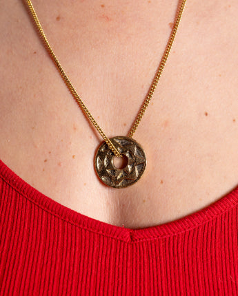 Gold necklace with a circular pendant on a person wearing a red garment.