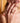 Close-up of a woman's hand with gold rings, wearing a red top against a blurred background.