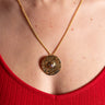 Gold necklace with a circular mixed metal pendant worn by a person in a red top.