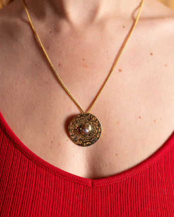 Gold necklace with a circular mixed metal pendant worn by a person in a red top.