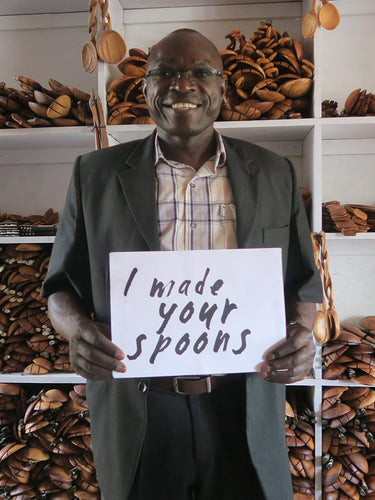 Man holding a sign saying 'I made your spoons' in a wooden spoon shop.